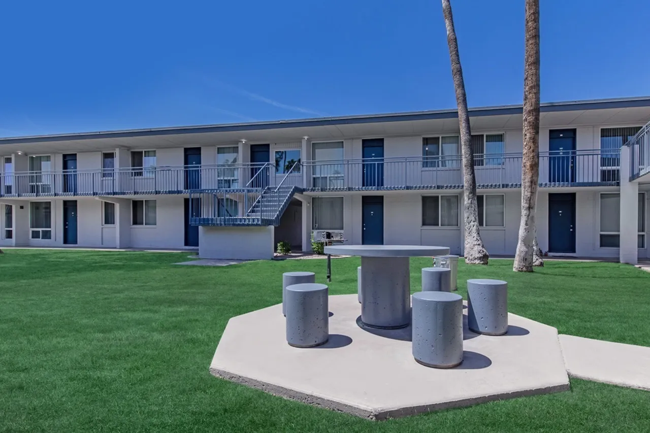 Courtyard with concrete seating area, green lawn, palm trees, two-story apartment building