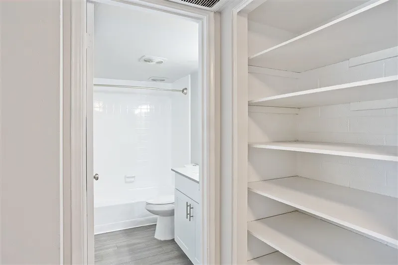 Bathroom with toilet, white cabinetry, wood-style plank flooring, linen closet with shelving