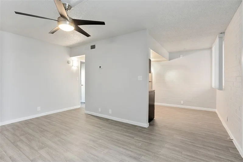 Living room, wood-style plank flooring, ceiling fan, white walls, entry door