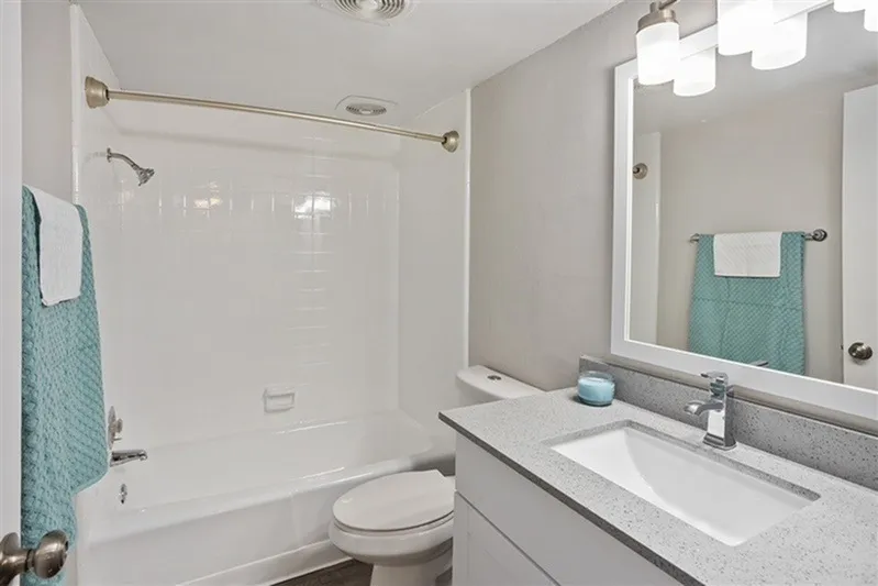 Bathroom with gray quartz countertops, white undermount sink, large mirror, white tile shower surround, turquoise towels