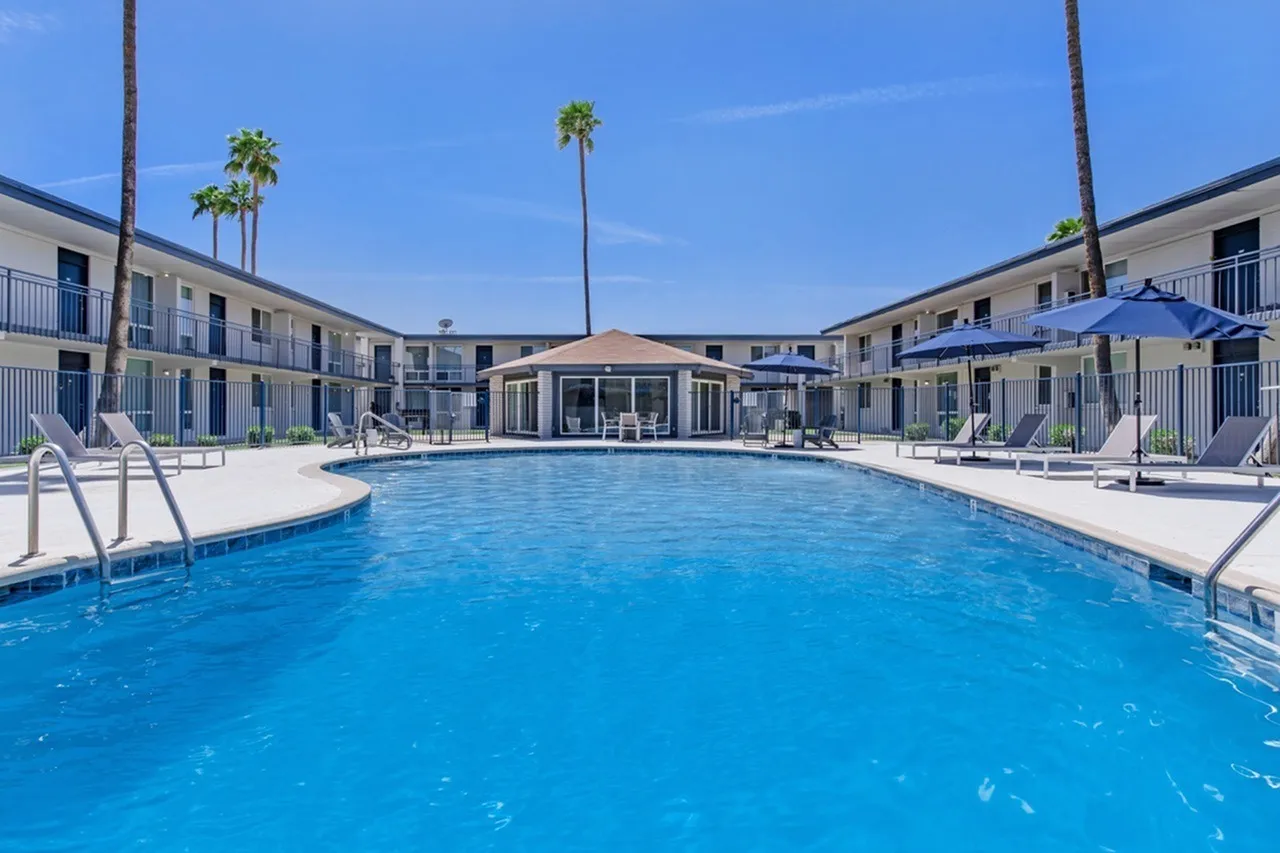 Sparkling blue resort pool, sunny seating areas, palm trees, apartment buildings