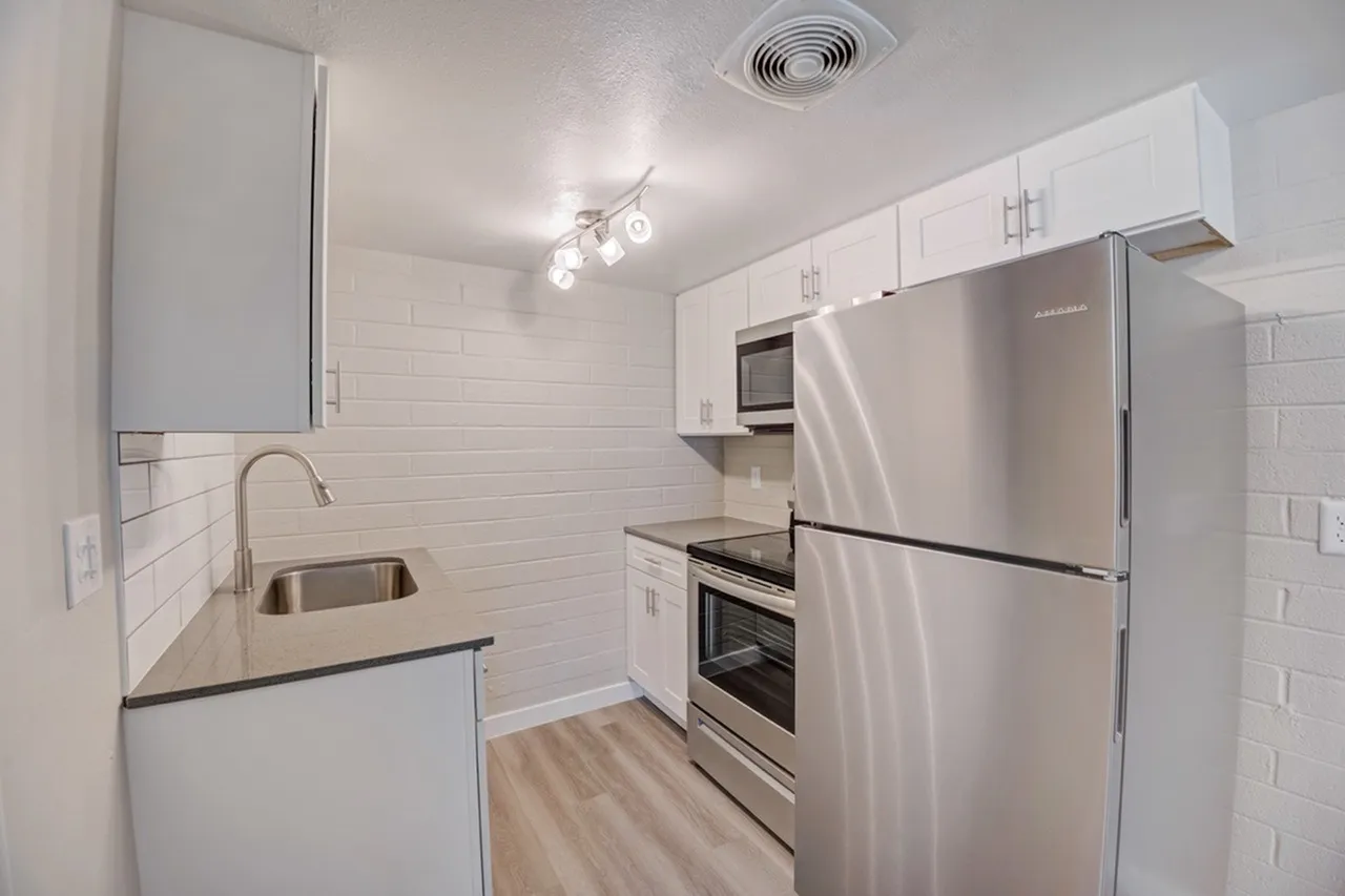 Kitchen, white shaker cabinetry, stainless steel appliances, black countertops, subway tile backsplash, wood-style plank flooring