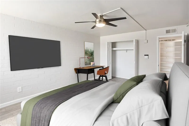 Primary bedroom, wood-style plank flooring, ceiling fan, wall-mounted TV, desk area