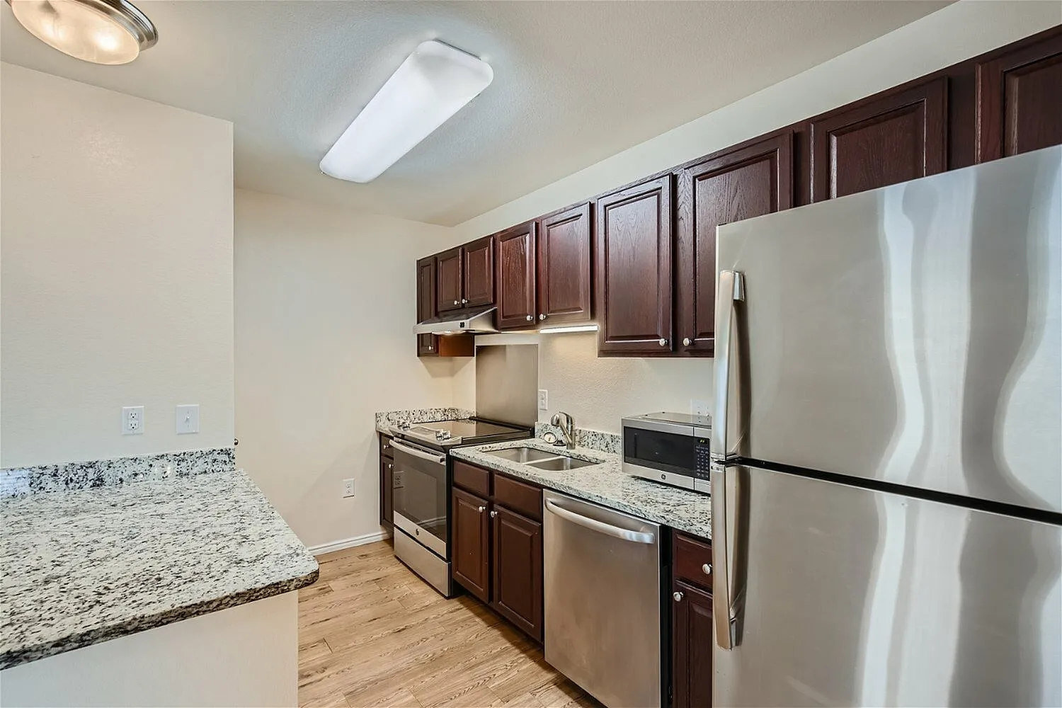 Kitchen, dark wood cabinetry, granite countertops, stainless appliances, wood-style plank flooring