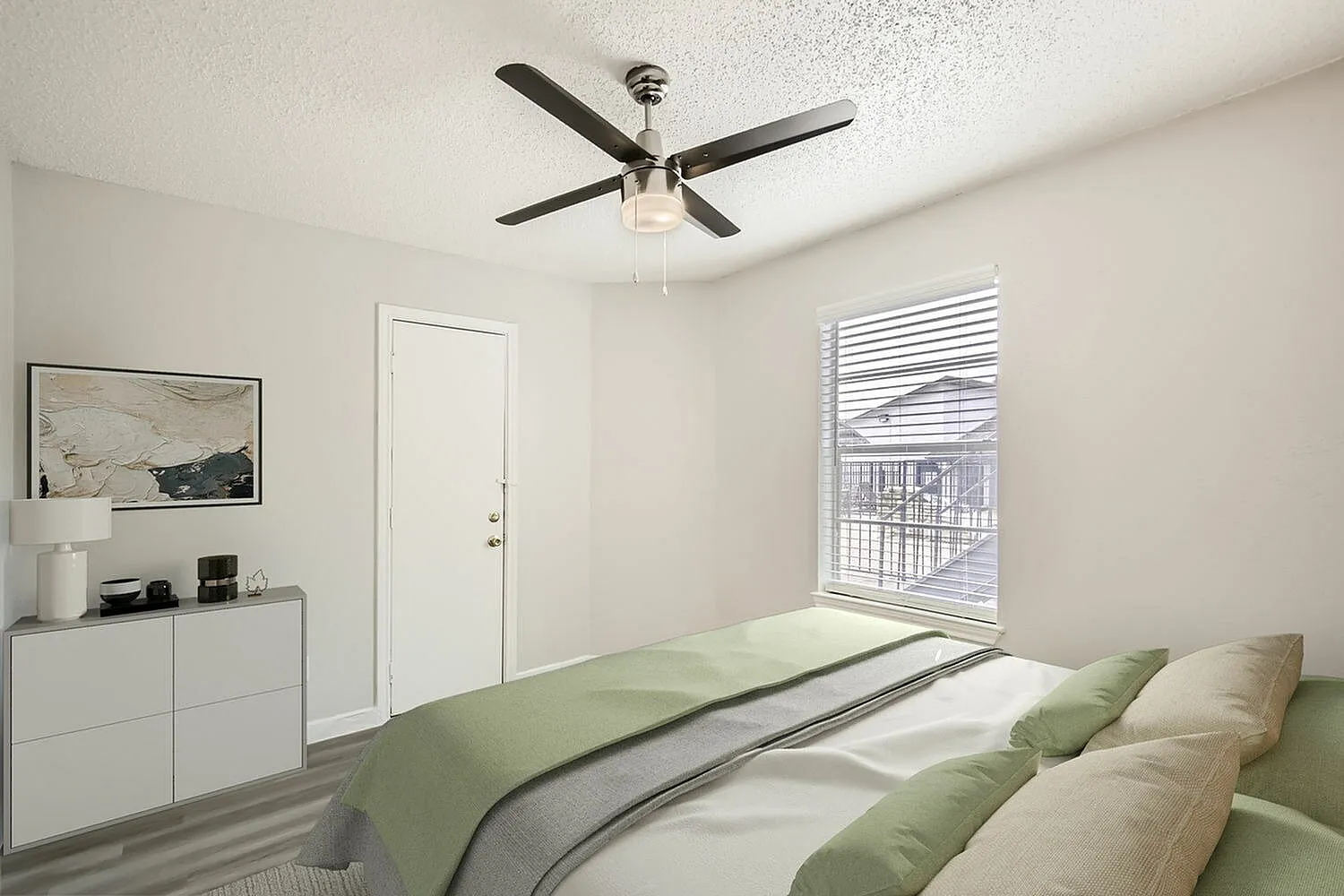 Primary bedroom, ceiling fan, white dresser with framed art, green bedding, window blinds