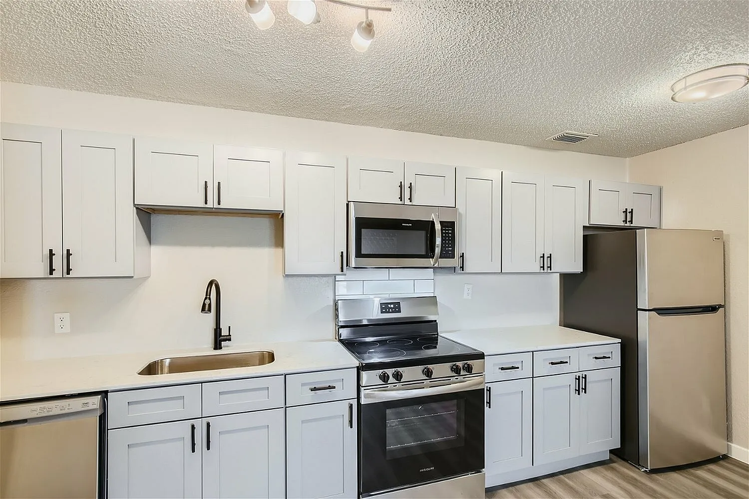 Kitchen, white shaker cabinetry, white subway tile backsplash, stainless steel appliances, wood-style plank flooring