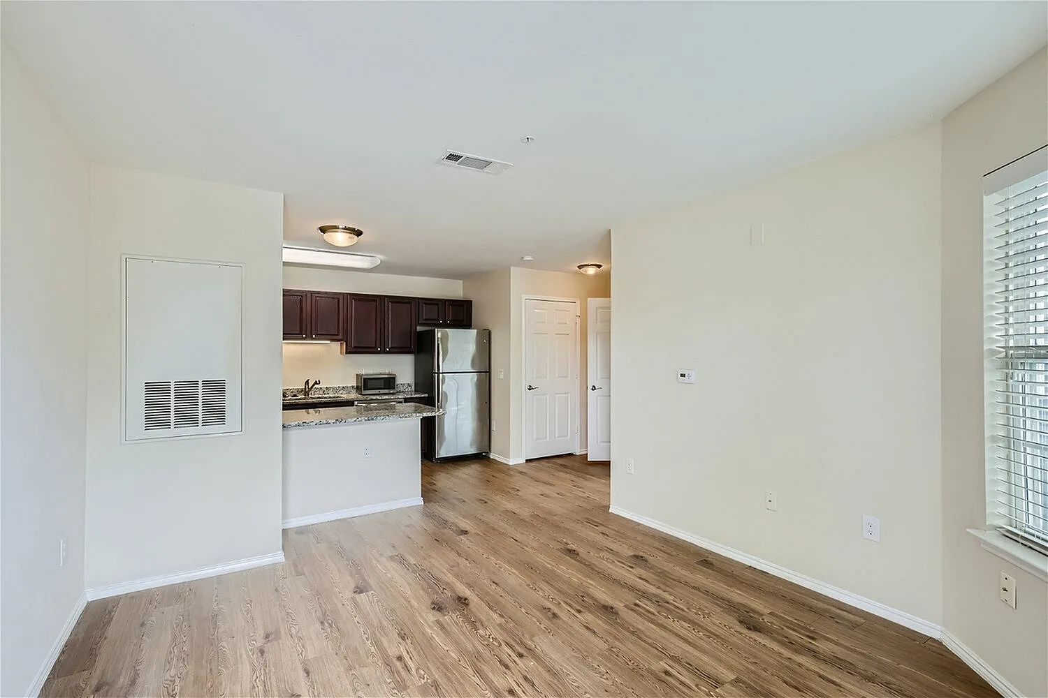 Living room with wood-style plank flooring, kitchen with dark cabinetry, granite countertops, stainless appliances