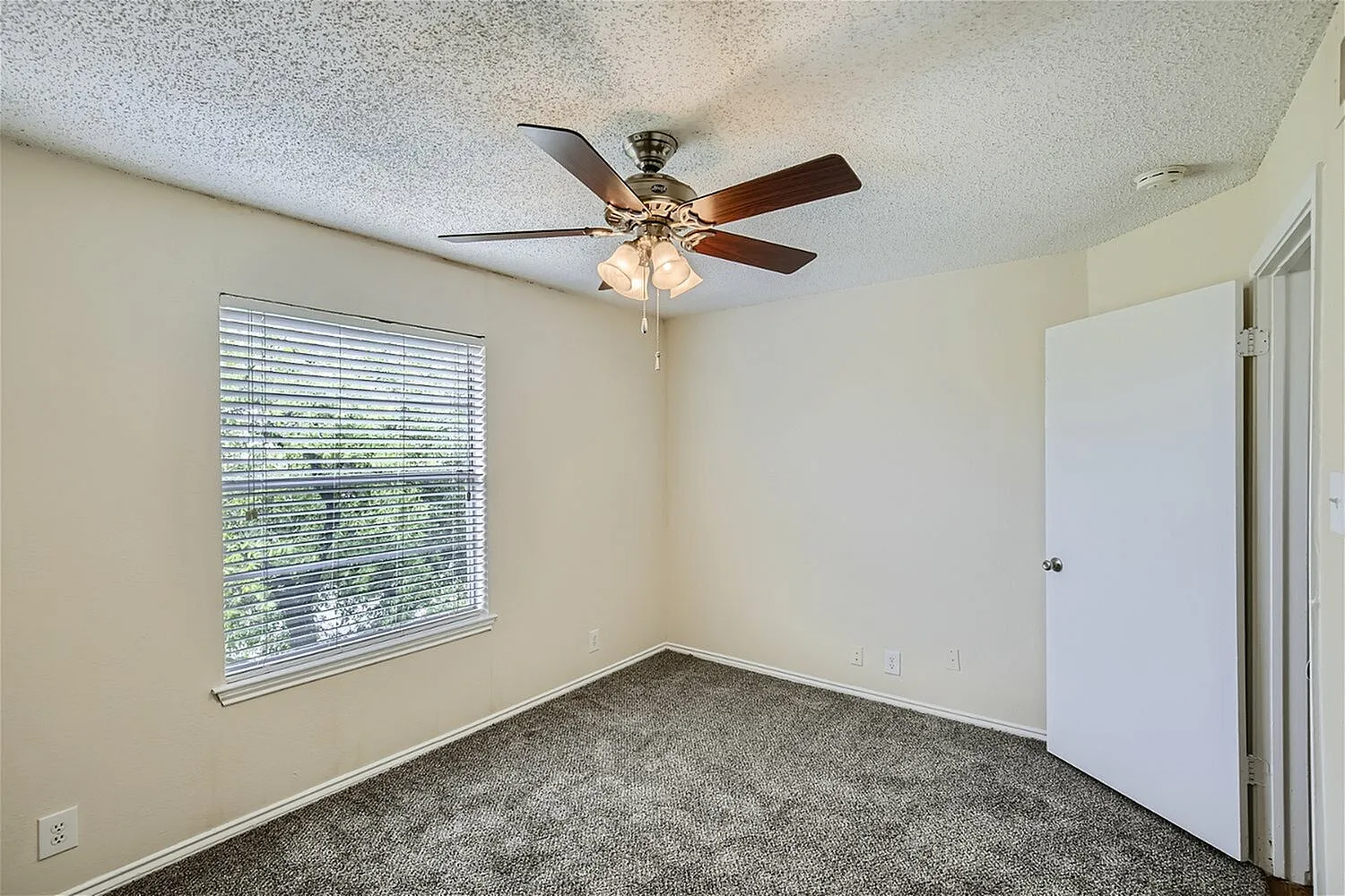 Bedroom, gray carpet flooring, ceiling fan with light fixture, large window with blinds, white closet door