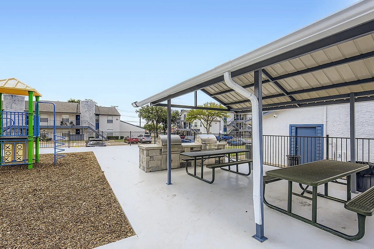 Covered patio with metal picnic tables, pergola structure, concrete flooring, playground visible