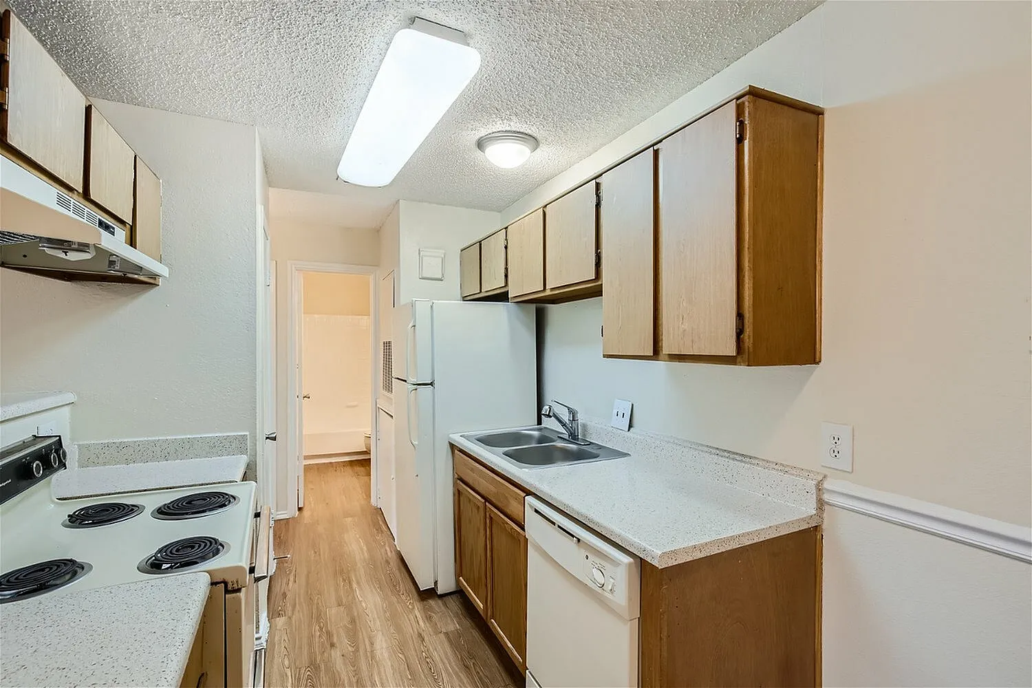 Galley kitchen, wood-style cabinetry, laminate countertops, white coil-top electric range, refrigerator, wood-style plank flooring