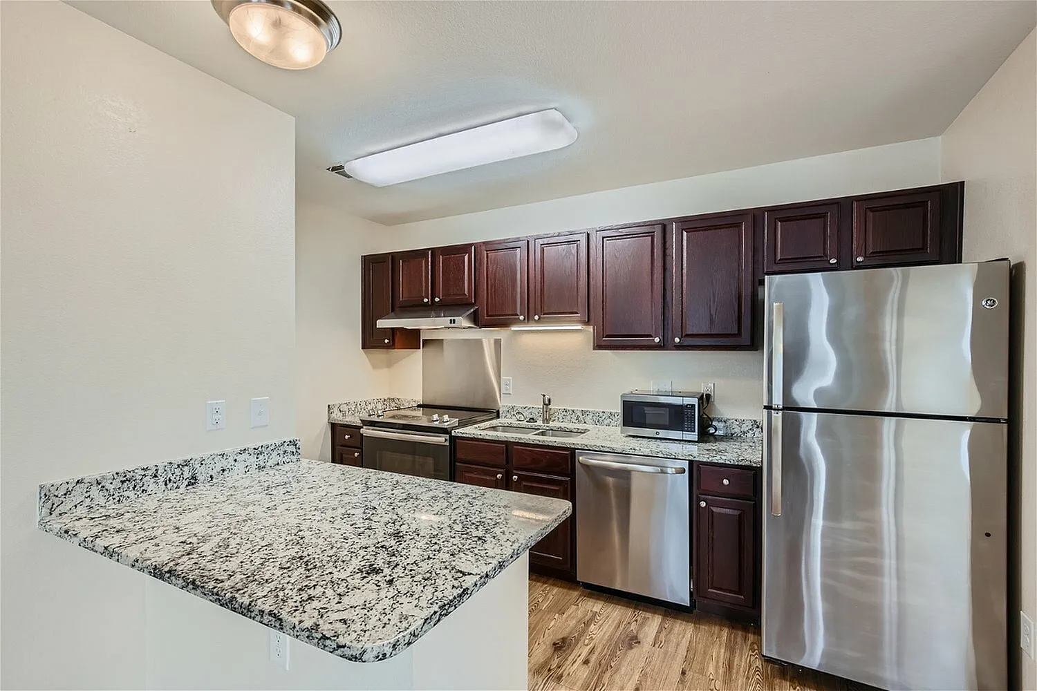 Kitchen, dark wood cabinetry, speckled quartz countertops, stainless steel appliances, wood-style plank flooring