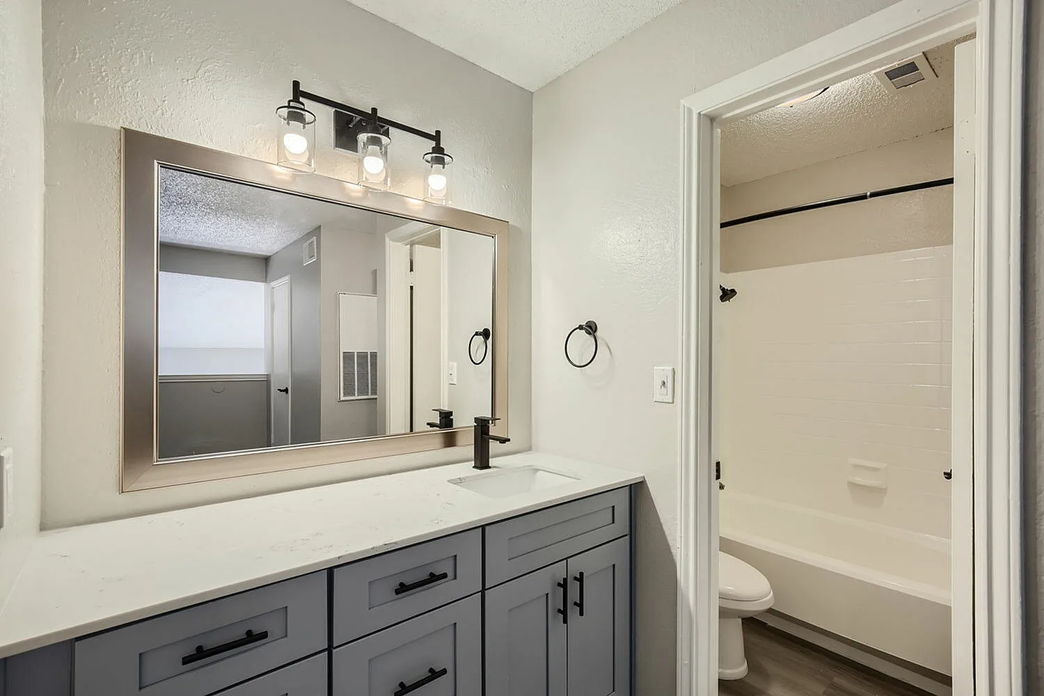 Primary bathroom, gray cabinetry, white quartz countertop, framed mirror, black vanity lighting fixtures