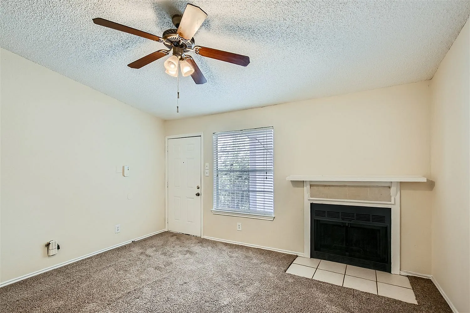 Living room with wood-style plank flooring, ceiling fan with light, entry door, fireplace