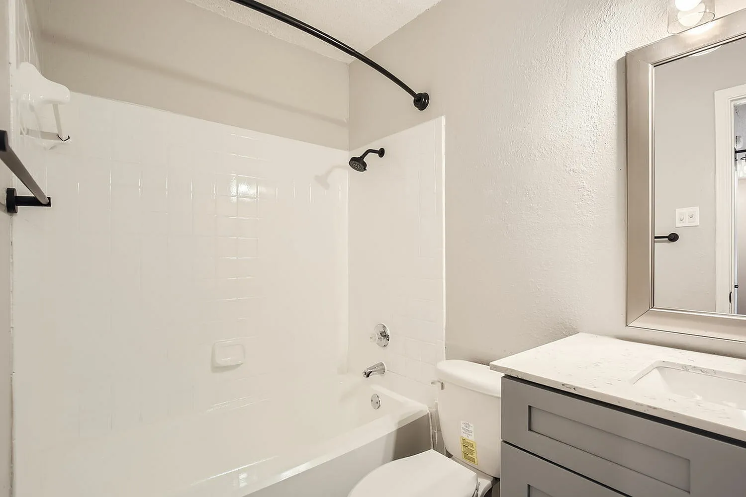 Bathroom, gray vanity cabinetry, white quartz countertops, white subway tile surround, soaking tub with black fixtures