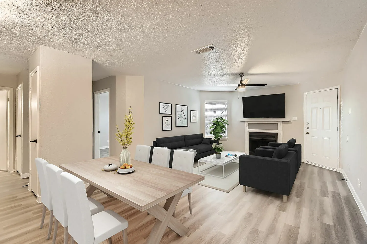 Open concept living and dining, wood-style plank flooring, black upholstered seating, wall-mounted TV