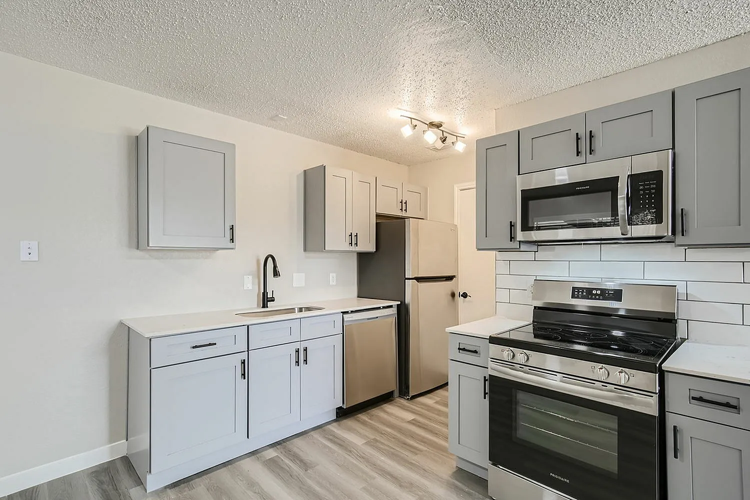 Kitchen, gray shaker cabinetry, white subway tile backsplash, stainless steel appliances, wood-style plank flooring