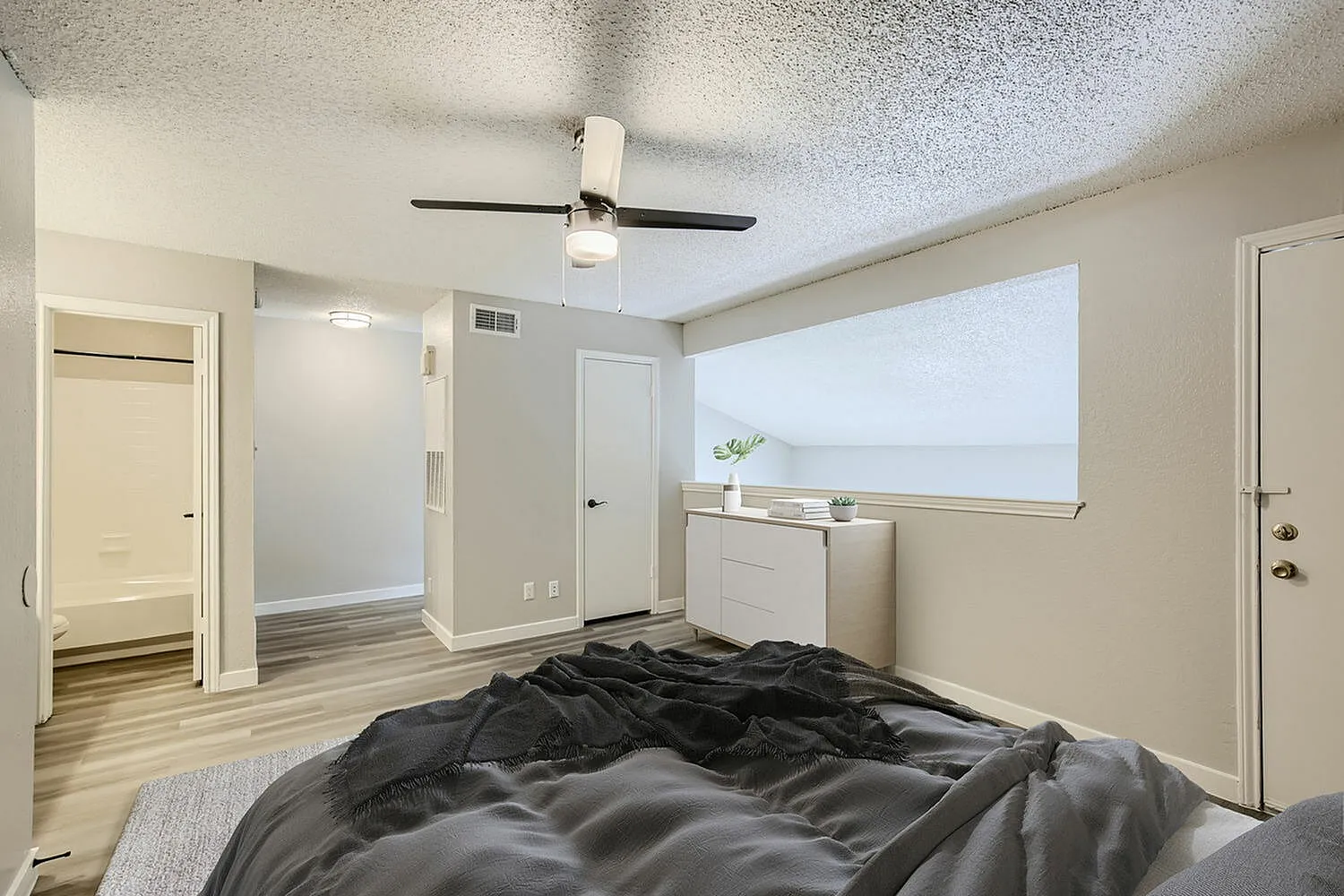 Primary bedroom, wood-style plank flooring, ceiling fan with black blades, window with roller shade