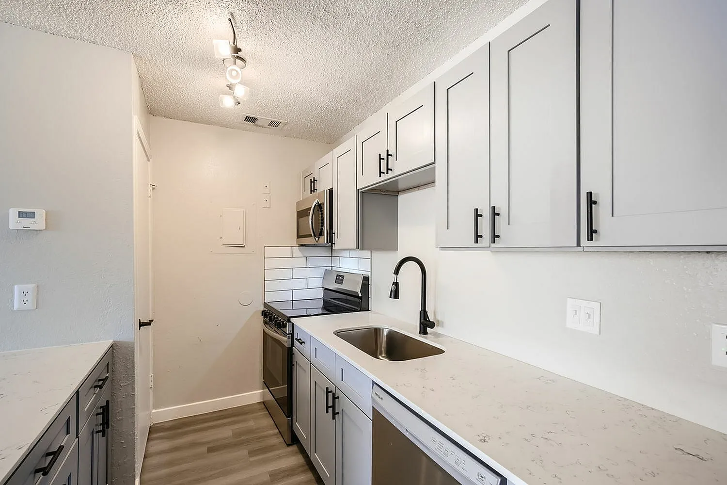 Kitchen, white shaker cabinetry, quartz countertops, stainless appliances, wood-style plank flooring