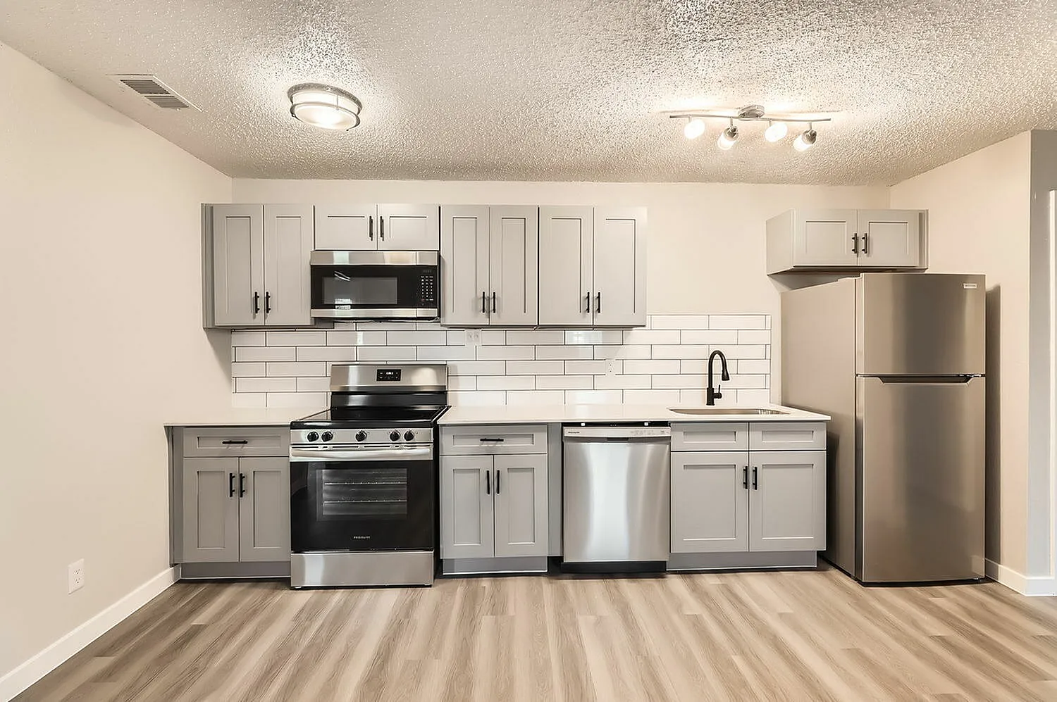 Kitchen, light gray cabinetry, white subway tile backsplash, stainless steel appliances, wood-style plank flooring