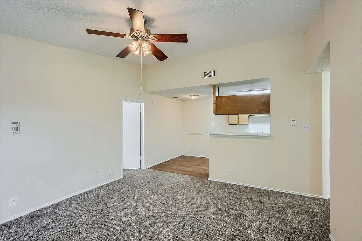 Living room, gray carpet flooring, ceiling fan with light fixture, wood-style plank accent wall, window