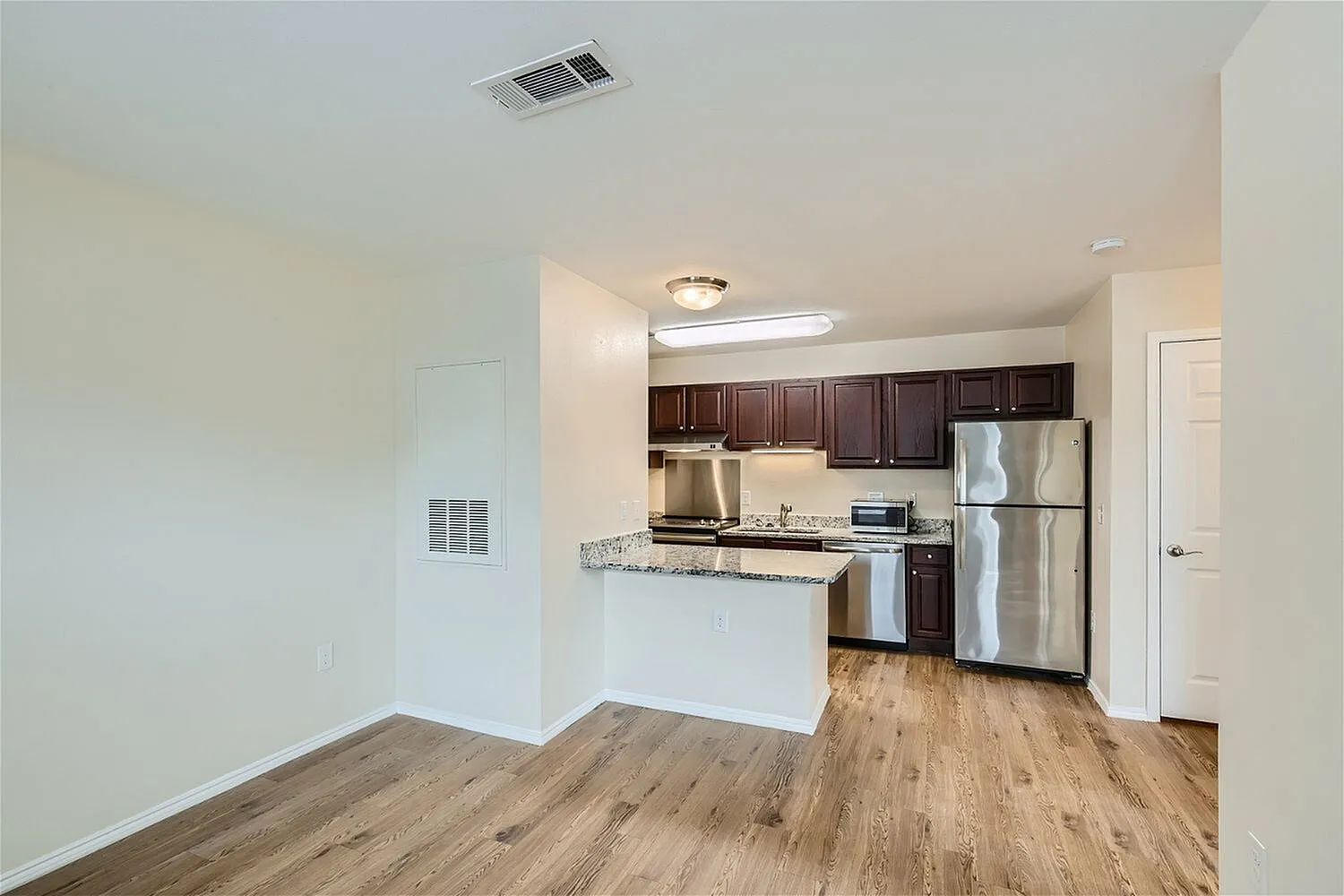 Kitchen and living room, dark wood cabinetry, granite countertops, stainless steel appliances, wood-style plank flooring