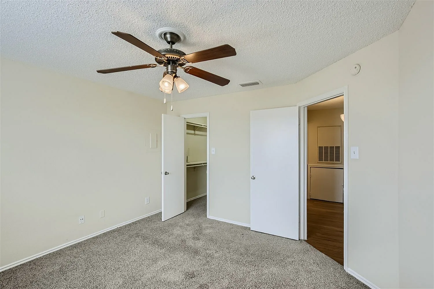 Bedroom, gray carpet flooring, ceiling fan with light fixture, two closets with white doors