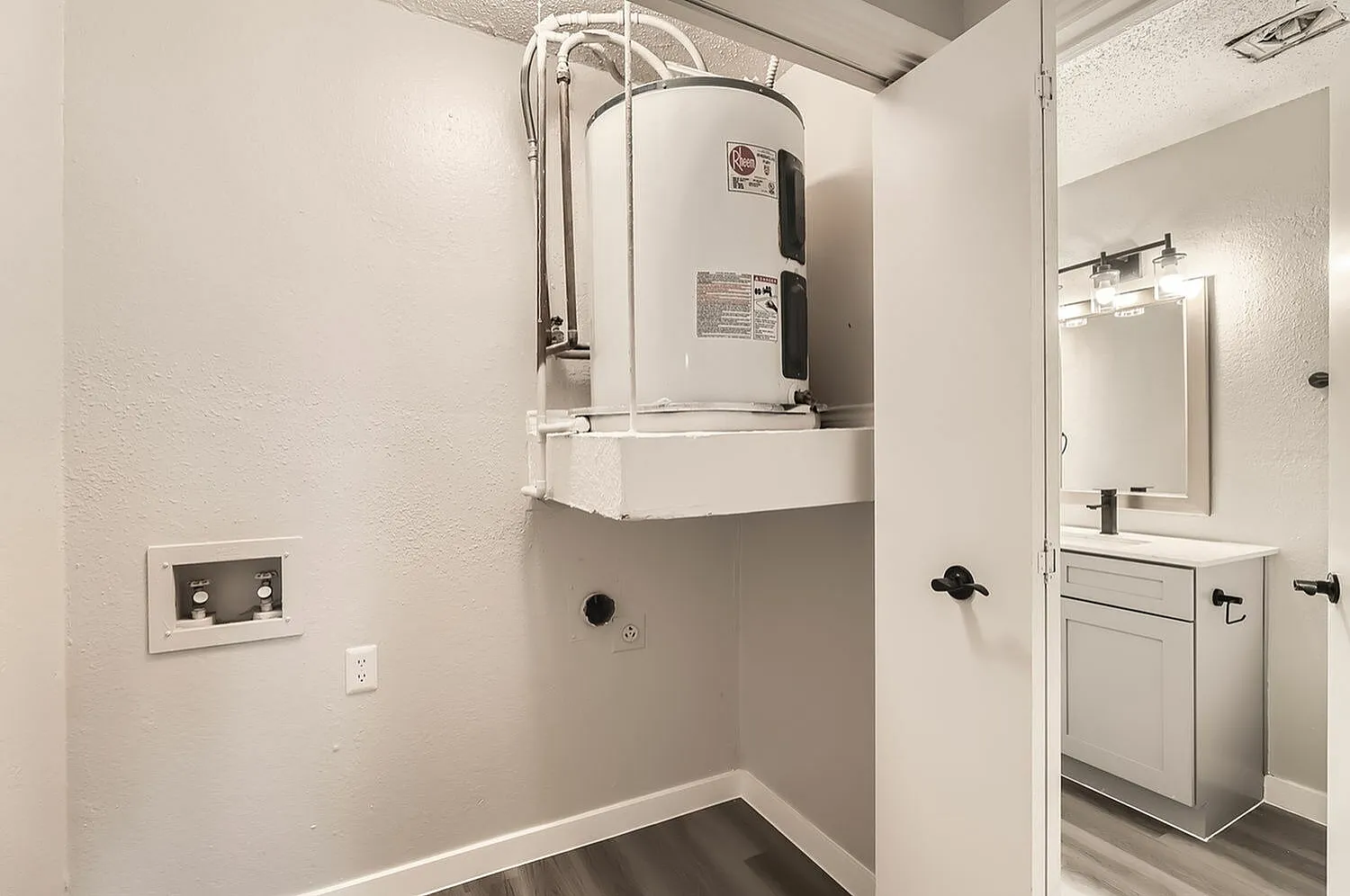 Utility room, wall-mounted water heater, electrical outlet, wood-style plank flooring
