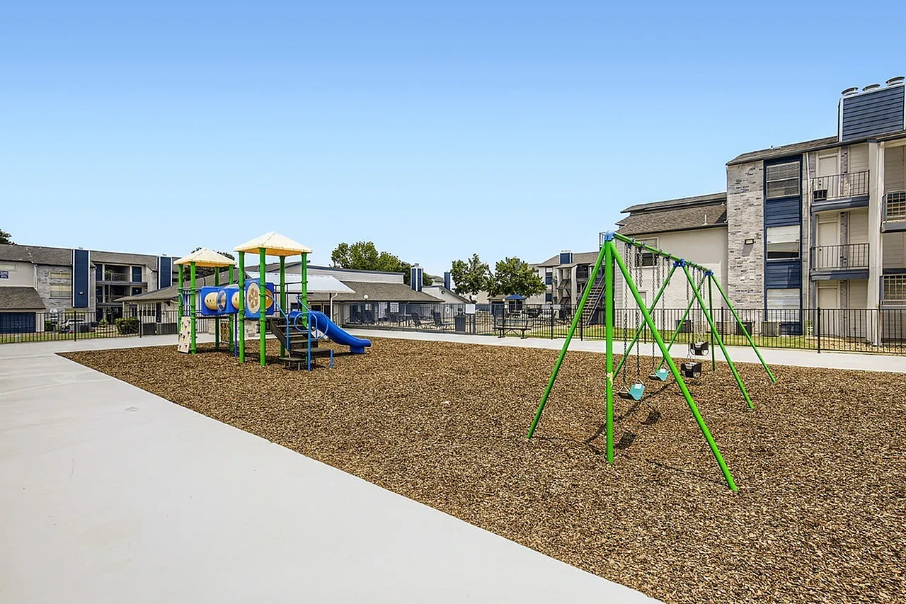 Playground, colorful play structures, mulch ground cover, concrete pathway, residential buildings