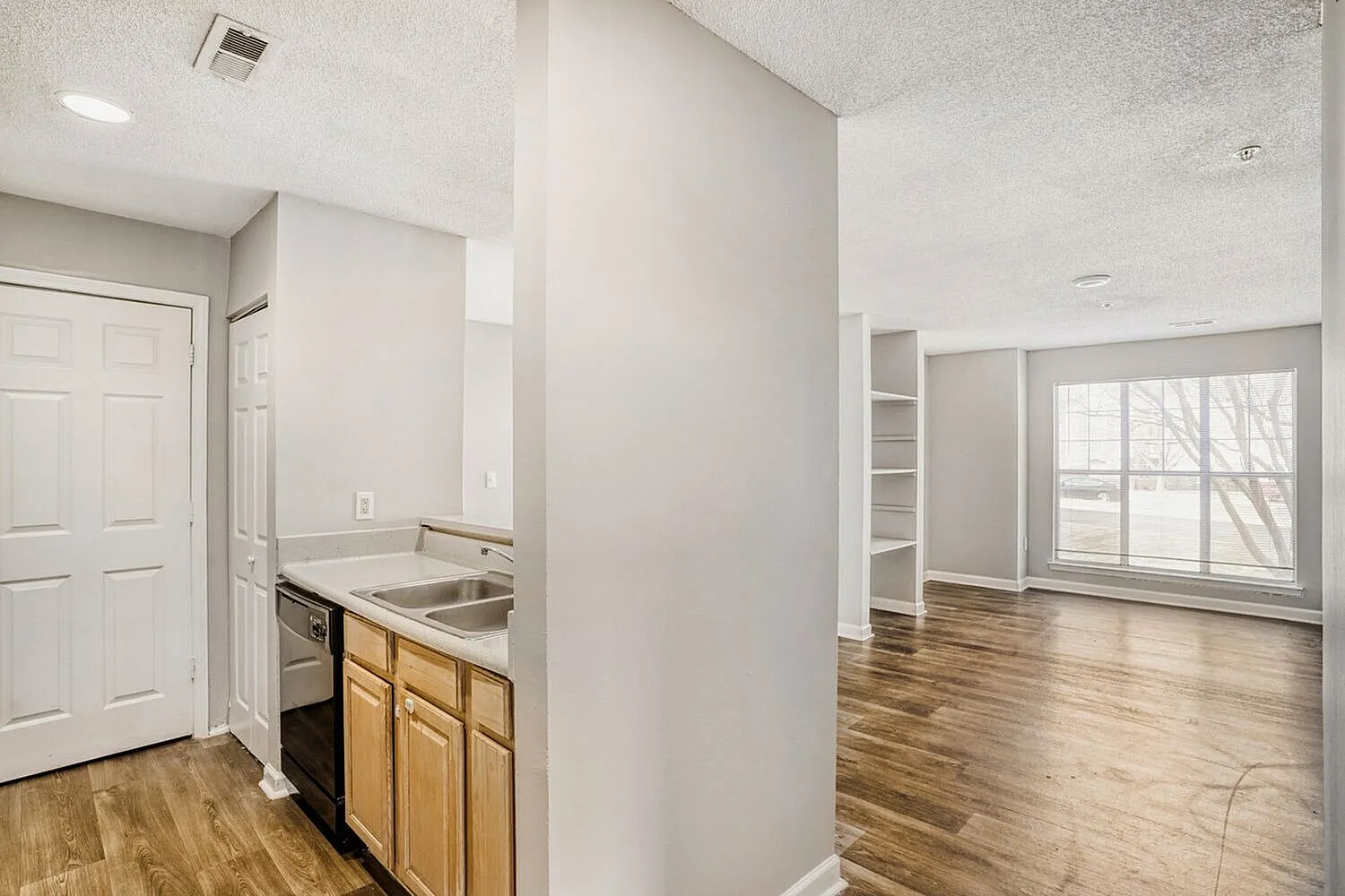 Kitchen with wood cabinetry, stainless sink, wood-style plank flooring, living room with large windows
