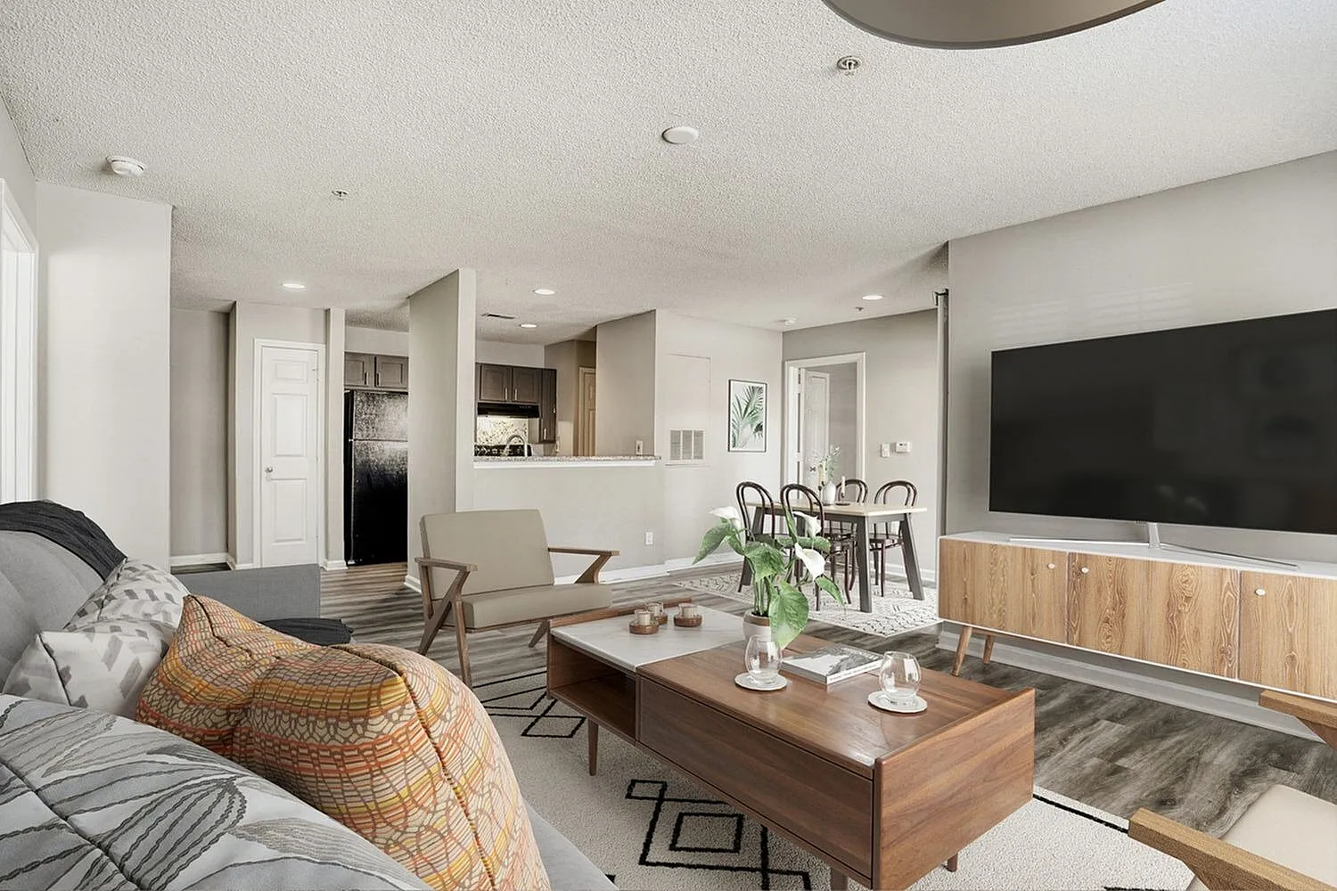 Living room, wood-style plank flooring, flat-screen TV, wood coffee table, kitchen island visible