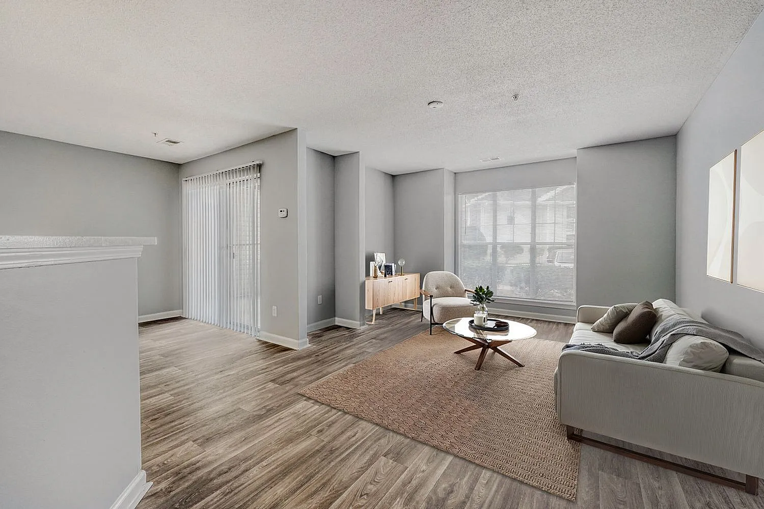 Living room, wood-style plank flooring, gray upholstered sofa, area rug, large windows, neutral décor