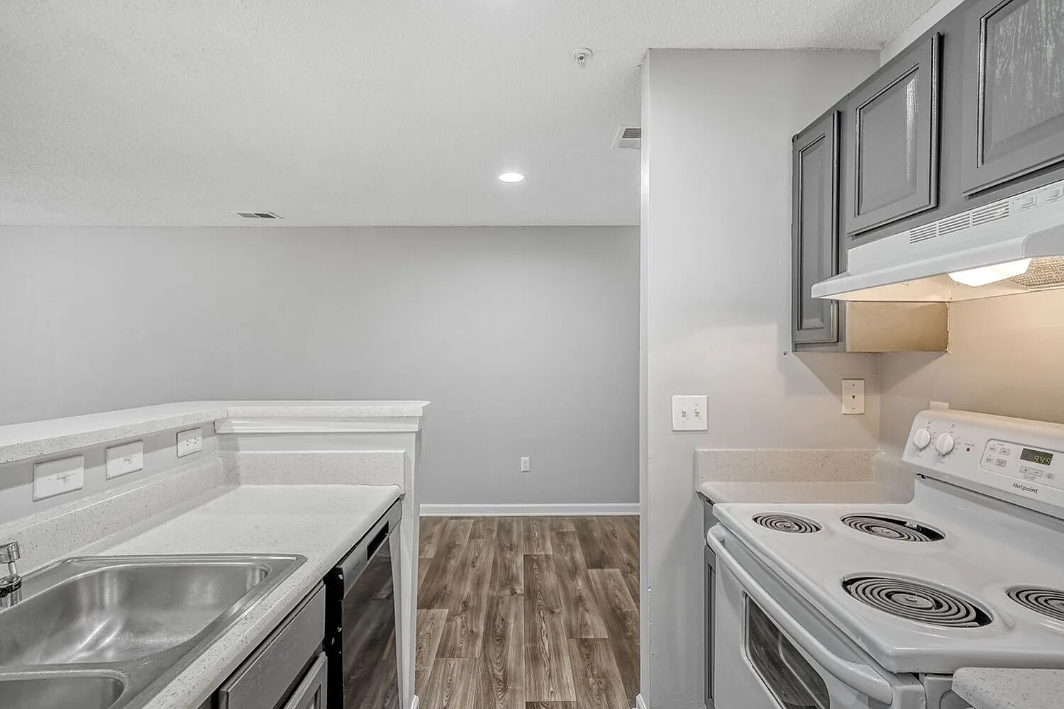 Kitchen with white cabinetry, stainless steel sink, white electric range, wood-style plank flooring, adjoining laundry space with white appliances