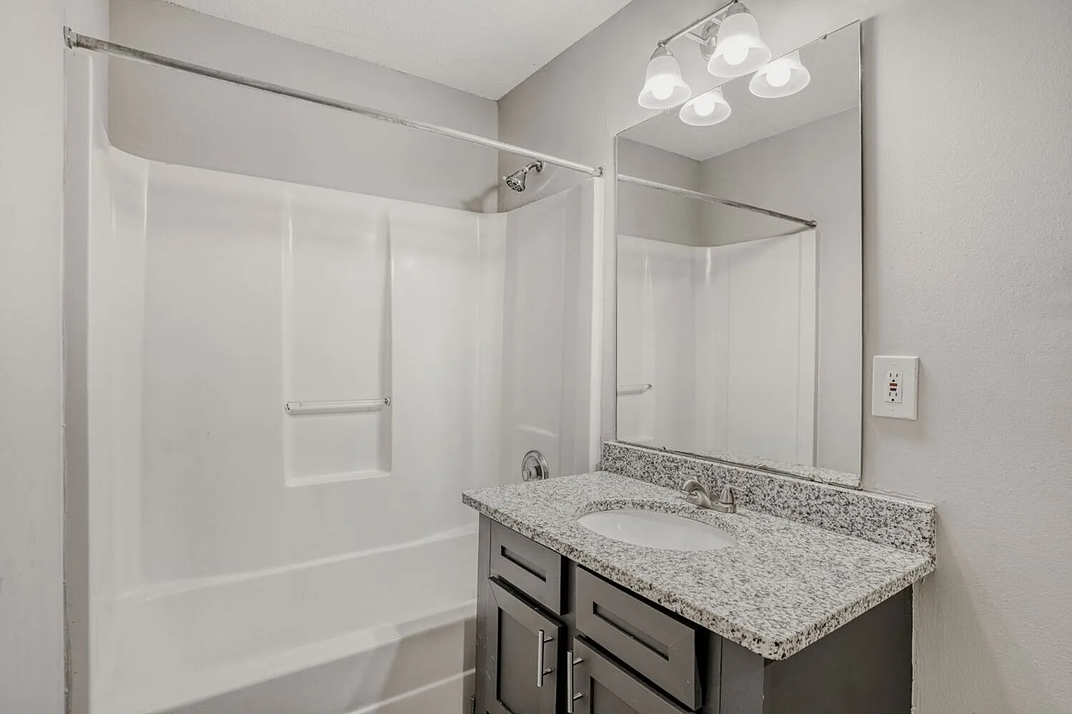 Bathroom, dark cabinetry, granite countertops, framed mirror, shower-tub combo