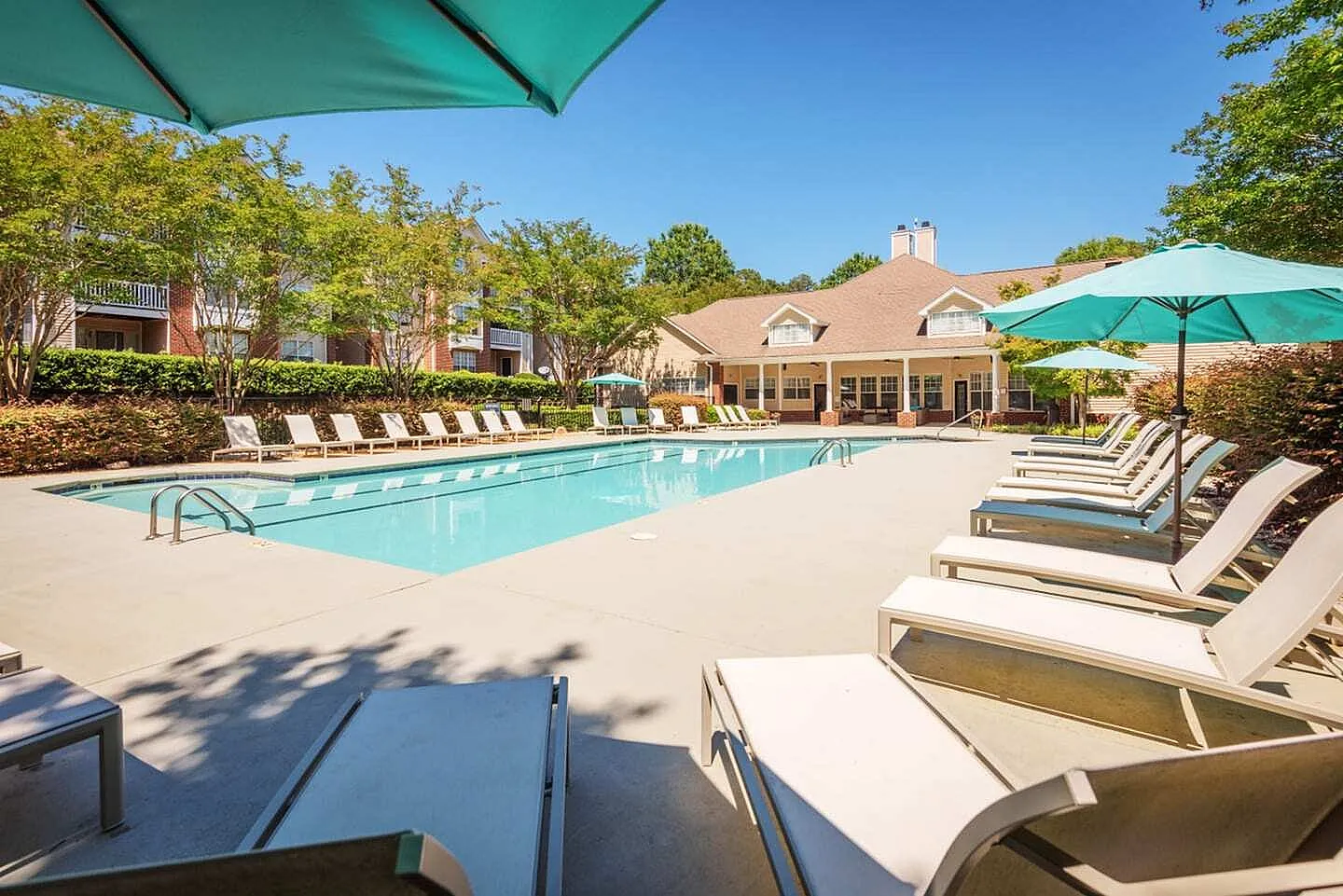 Resort-style swimming pool, lounge chairs, turquoise umbrellas, clubhouse