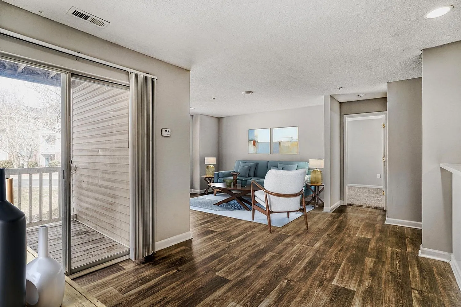 Living room with wood-style plank flooring, blue upholstered sofa, white armchair, sliding glass door with blinds