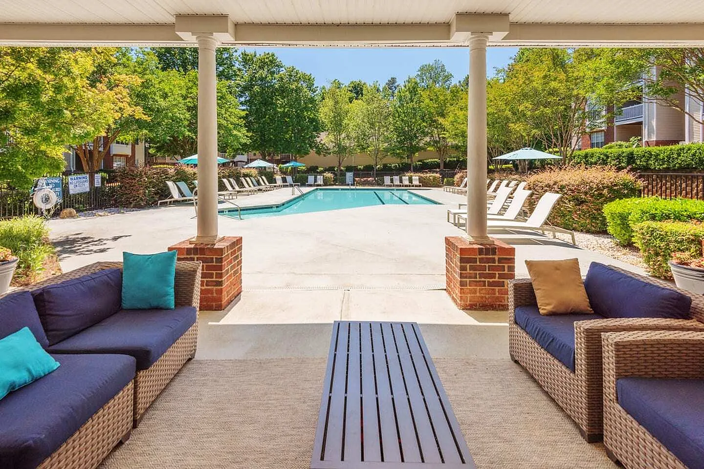 Pool deck with lounge seating, woven furniture, turquoise accents, shaded pergola