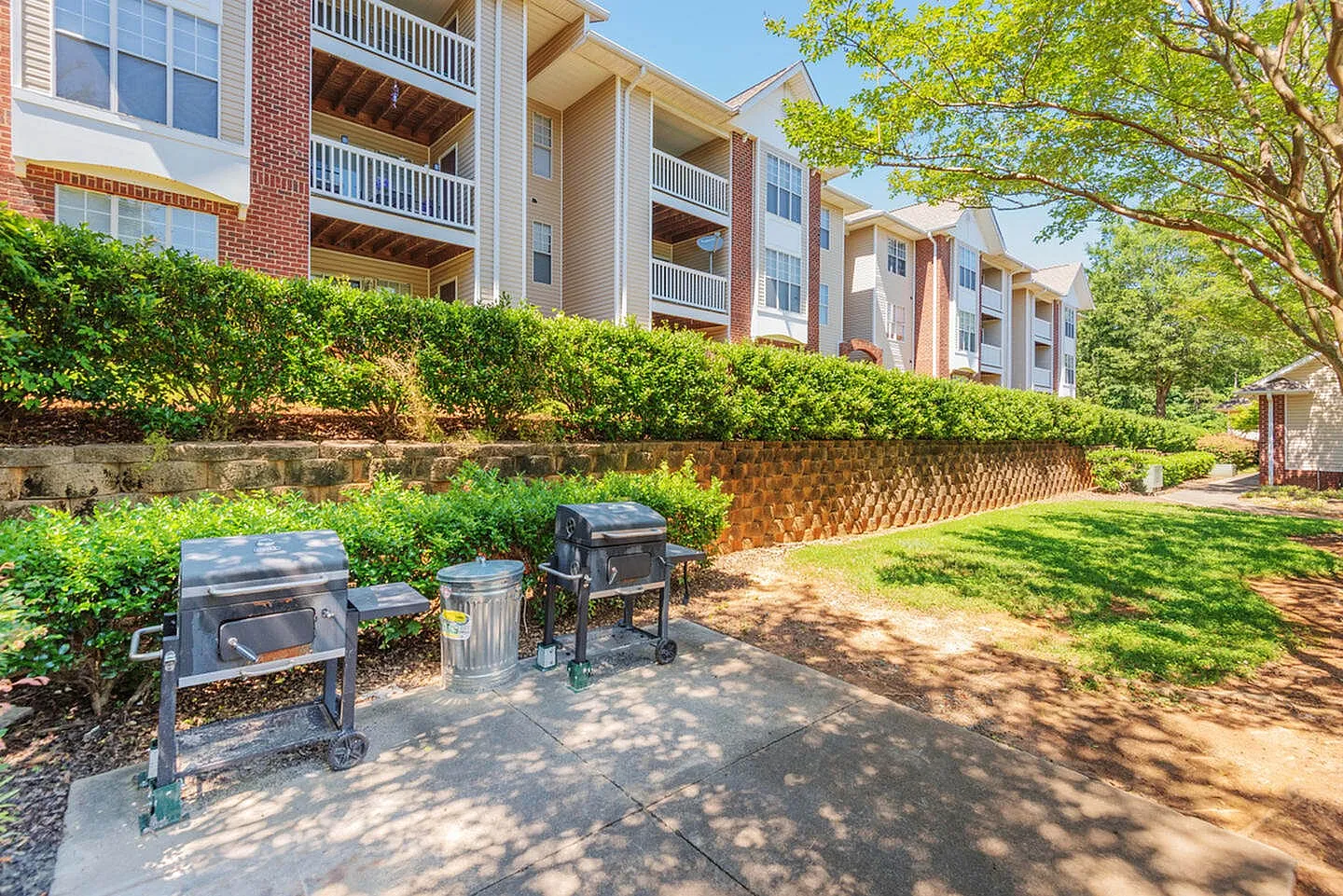 Outdoor grilling area, multiple grills, trash receptacle, manicured hedges, brick building