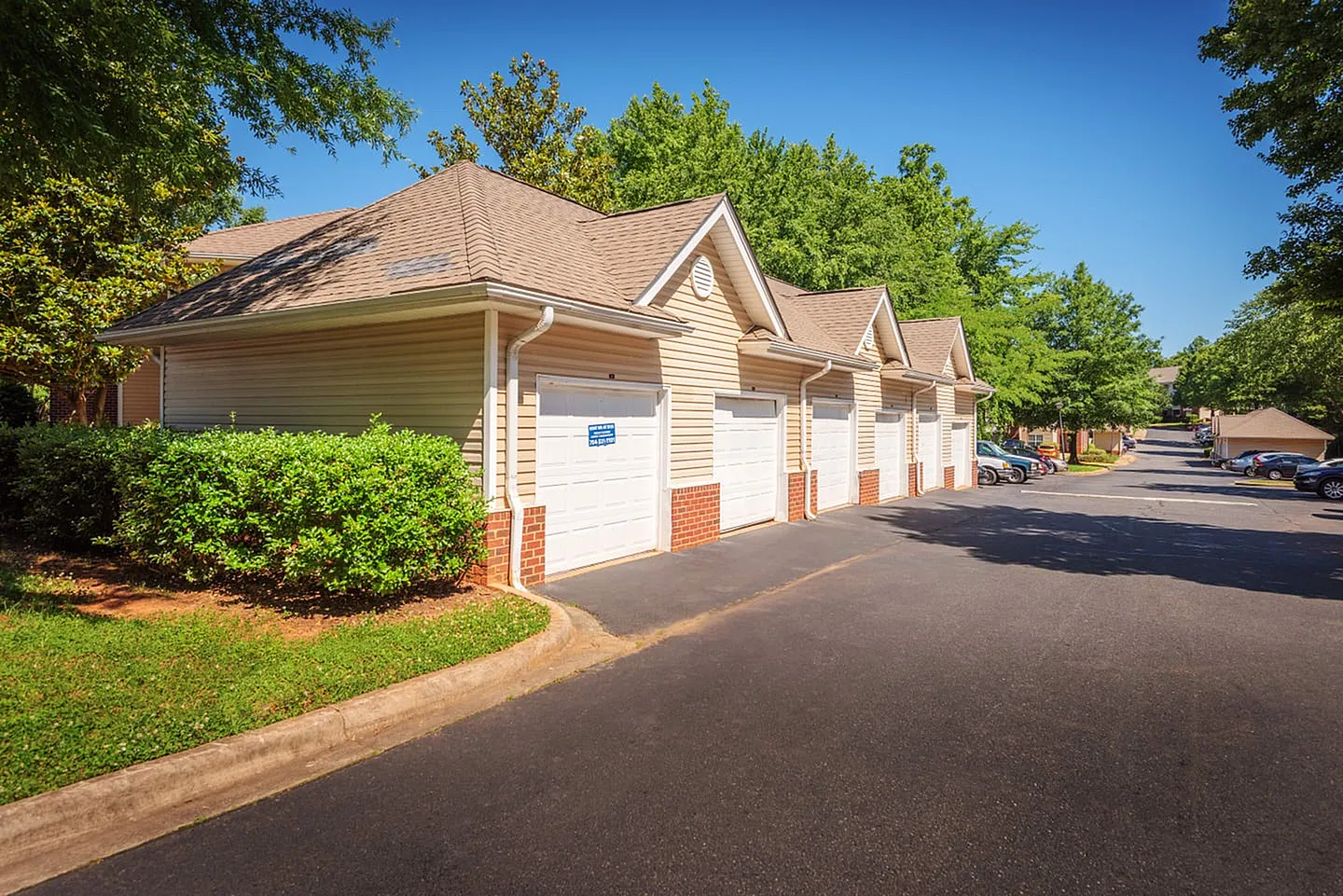 Garage building, white panel siding, brick base, pitched roof, white garage doors, landscaping, asphalt drive