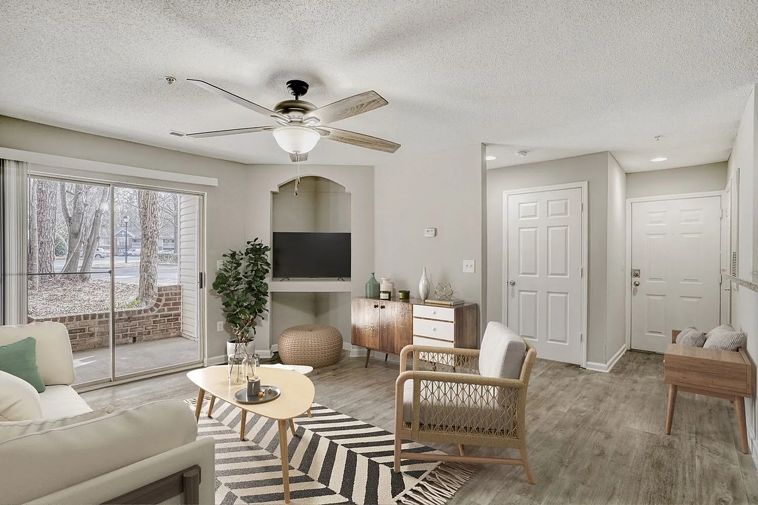 Living room, wood-style plank flooring, ceiling fan, fireplace with TV, patio doors