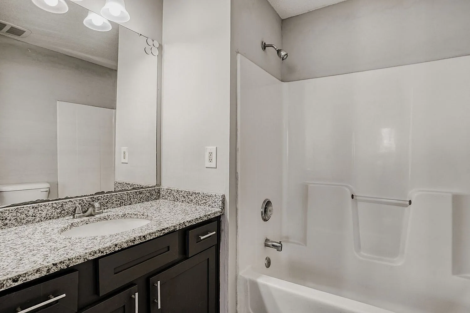 Primary bathroom, speckled gray quartz countertops, dark cabinetry, white subway tile surround