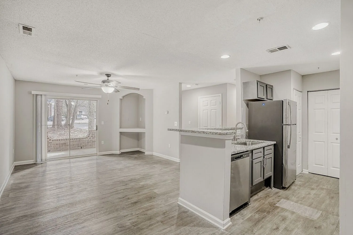 Kitchen with stainless appliances, white cabinetry, gray countertops, wood-style plank flooring, open living space with ceiling fan