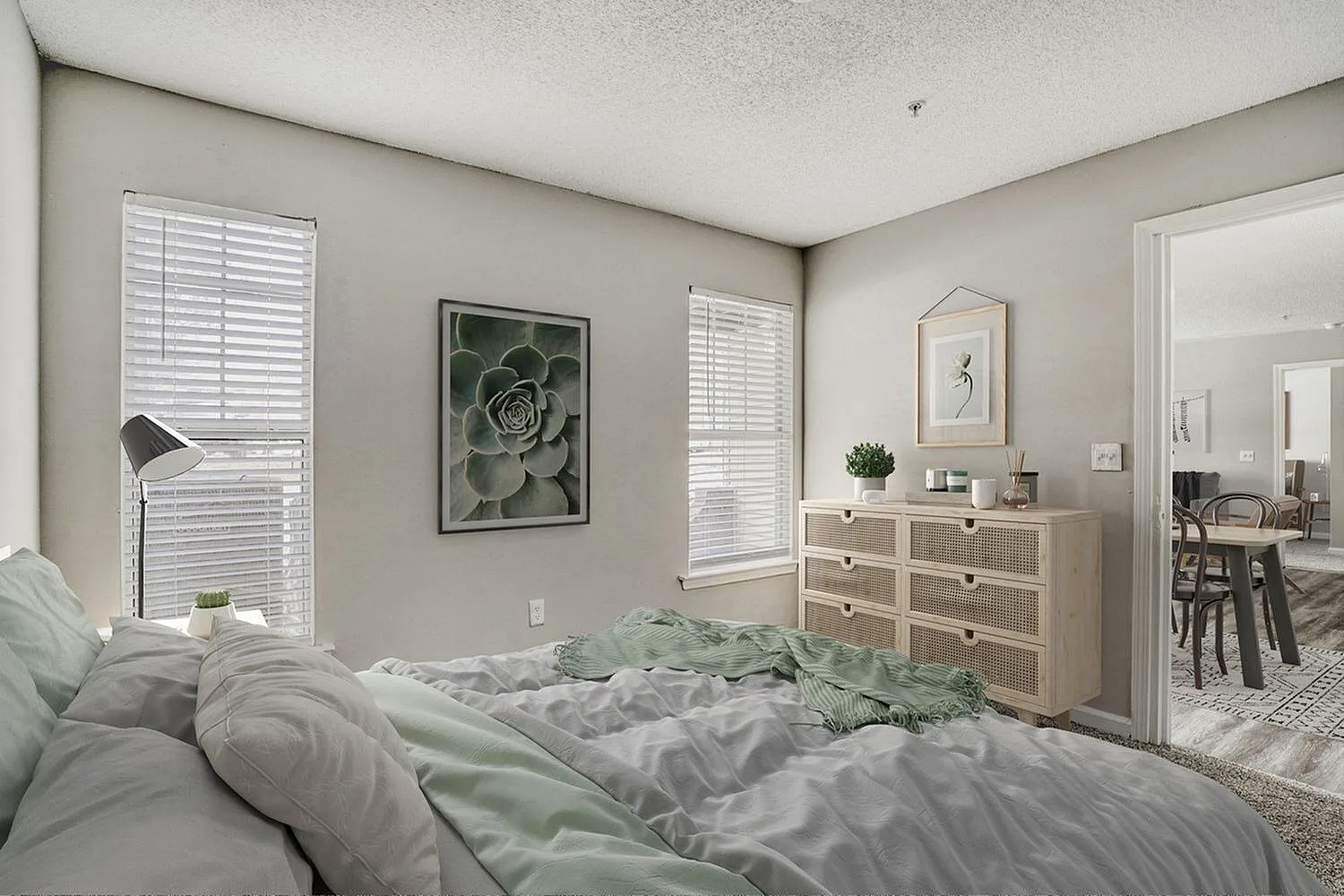Primary bedroom, gray bedding, wood-style dresser, white shutters, succulent plant, botanical wall art