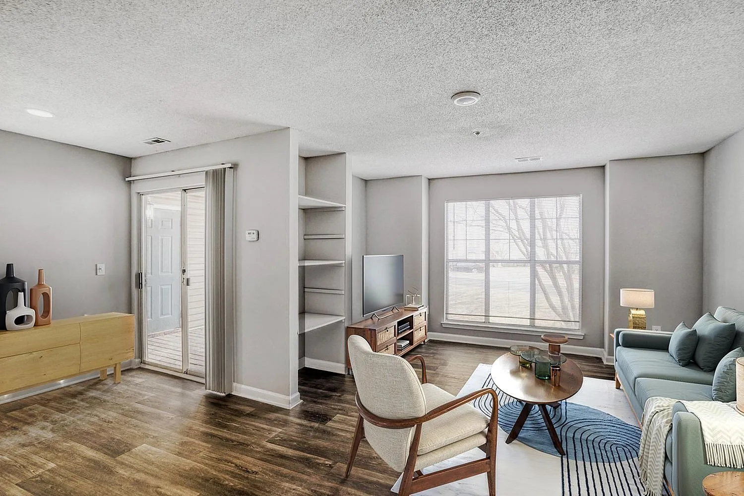 Studio living room, wood-style plank flooring, gray walls, large window, upholstered seating