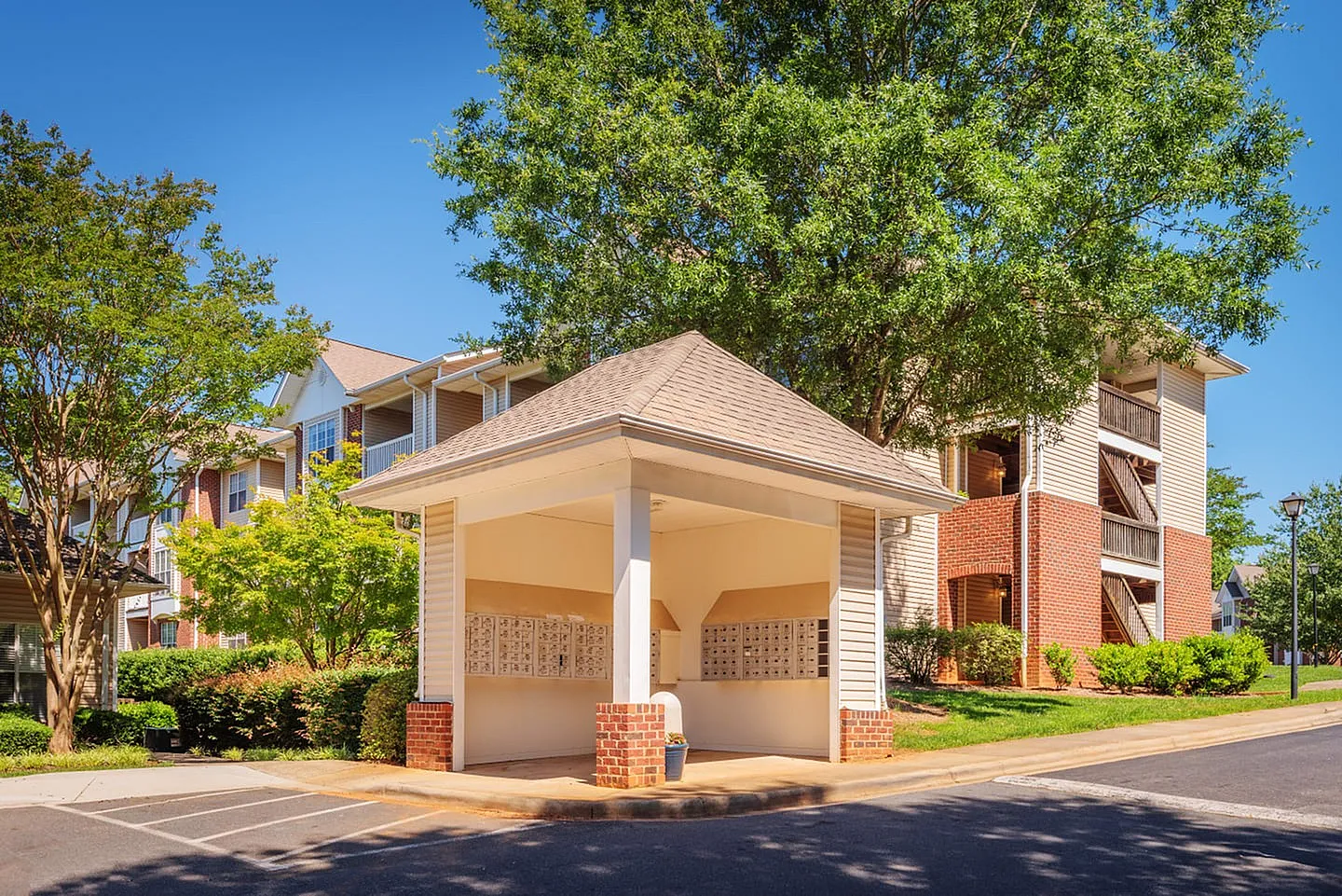 Covered carport with brick columns, residential building, mature trees, clear sky