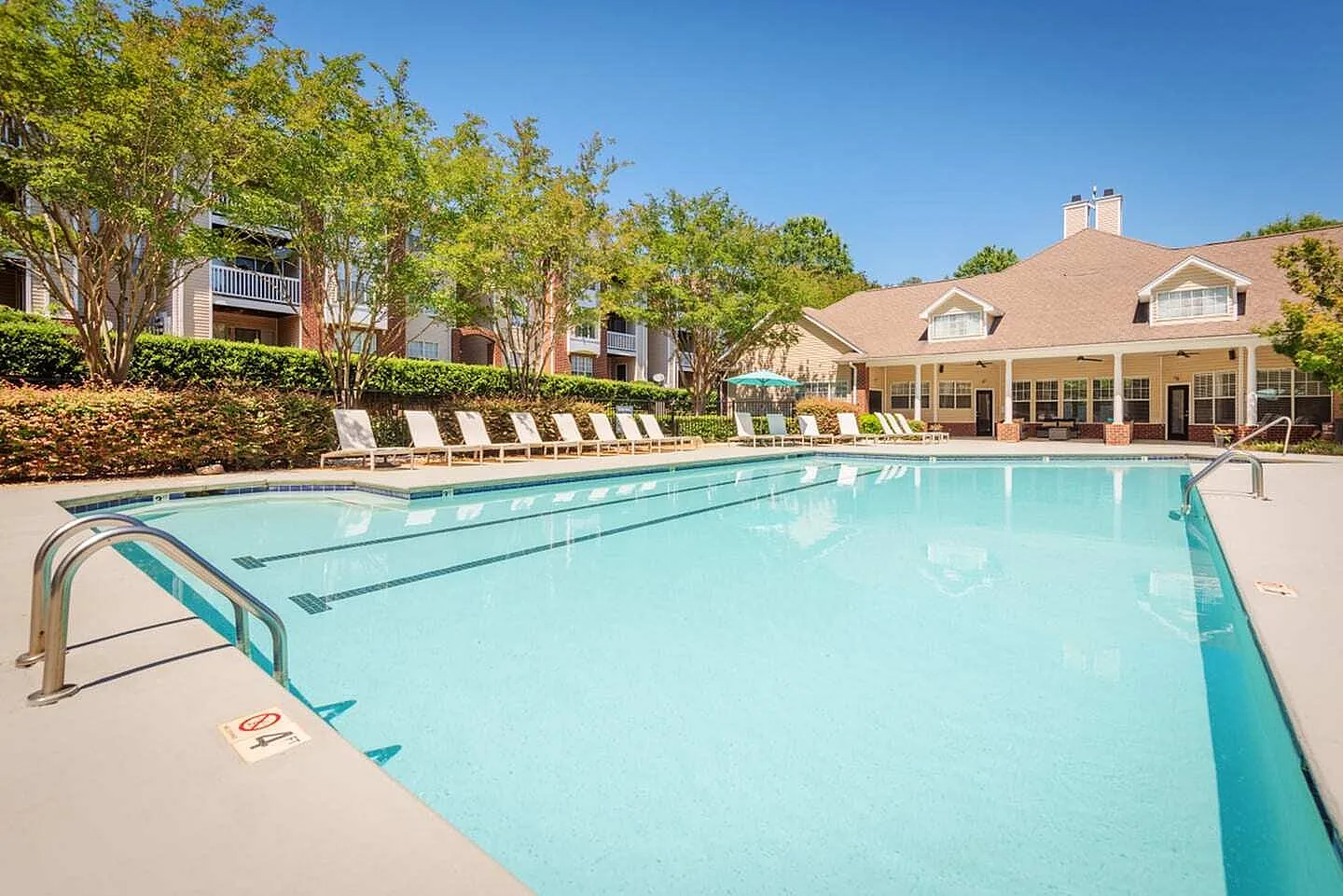 Resort pool with lane markings, lounge chairs, shade trees, residential buildings