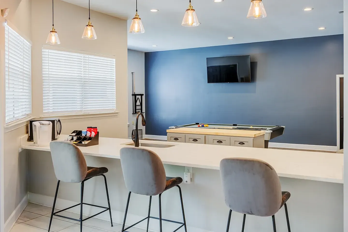 Game room, bar seating with upholstered chairs, pool table, blue accent wall, pendant lighting