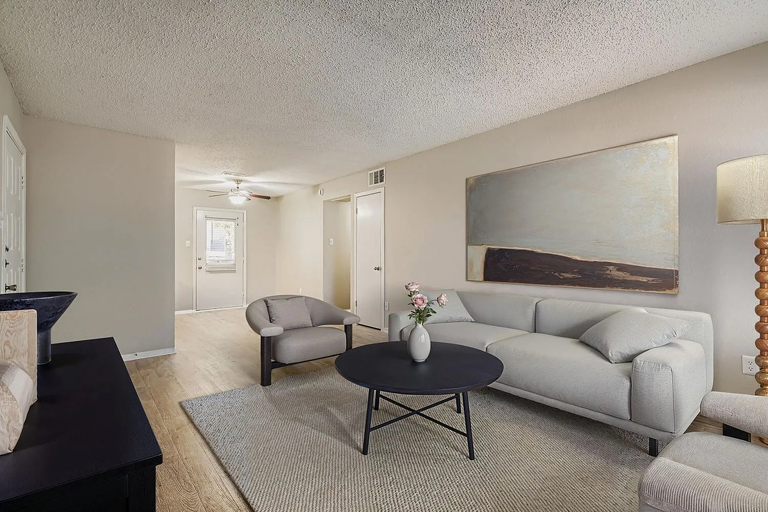 Living room with light gray sofa, accent chair, black round table, wood-style plank flooring, ceiling fan