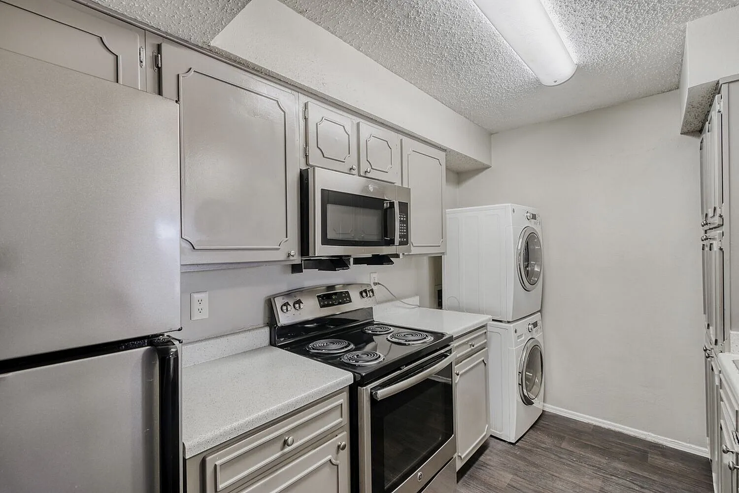 Kitchen, stainless steel appliances, white cabinetry, wood-style plank flooring, stacked washer and dryer