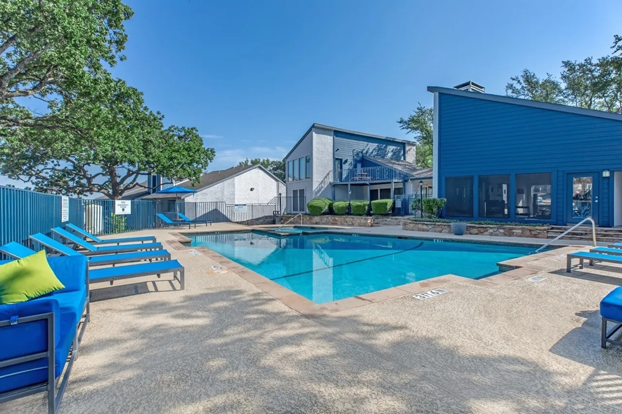 Resort-style swimming pool, blue lounge chairs, multi-level residential buildings, mature trees