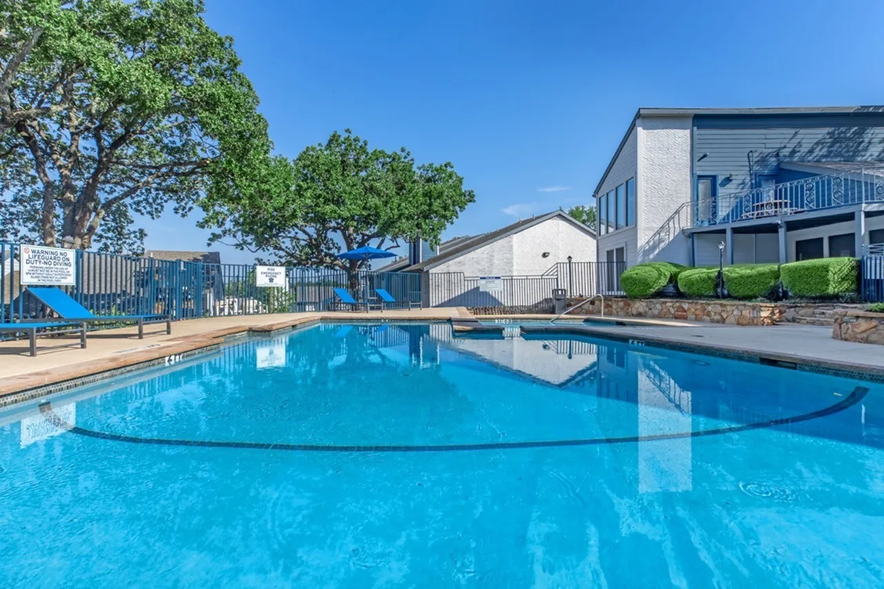 Swimming pool with turquoise water, lounge chairs, landscaping, residential buildings